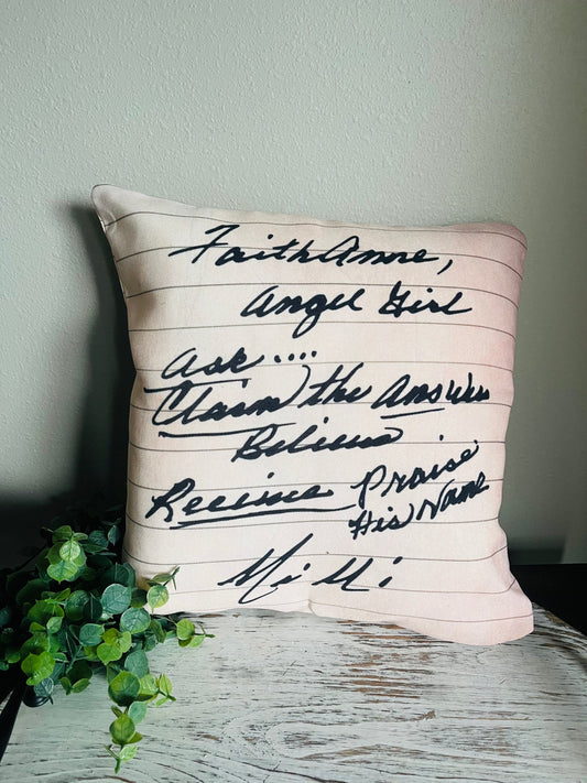 A custom pillowcase with handwritten text on a beige background, displayed on a wooden surface with a plant to the side.
